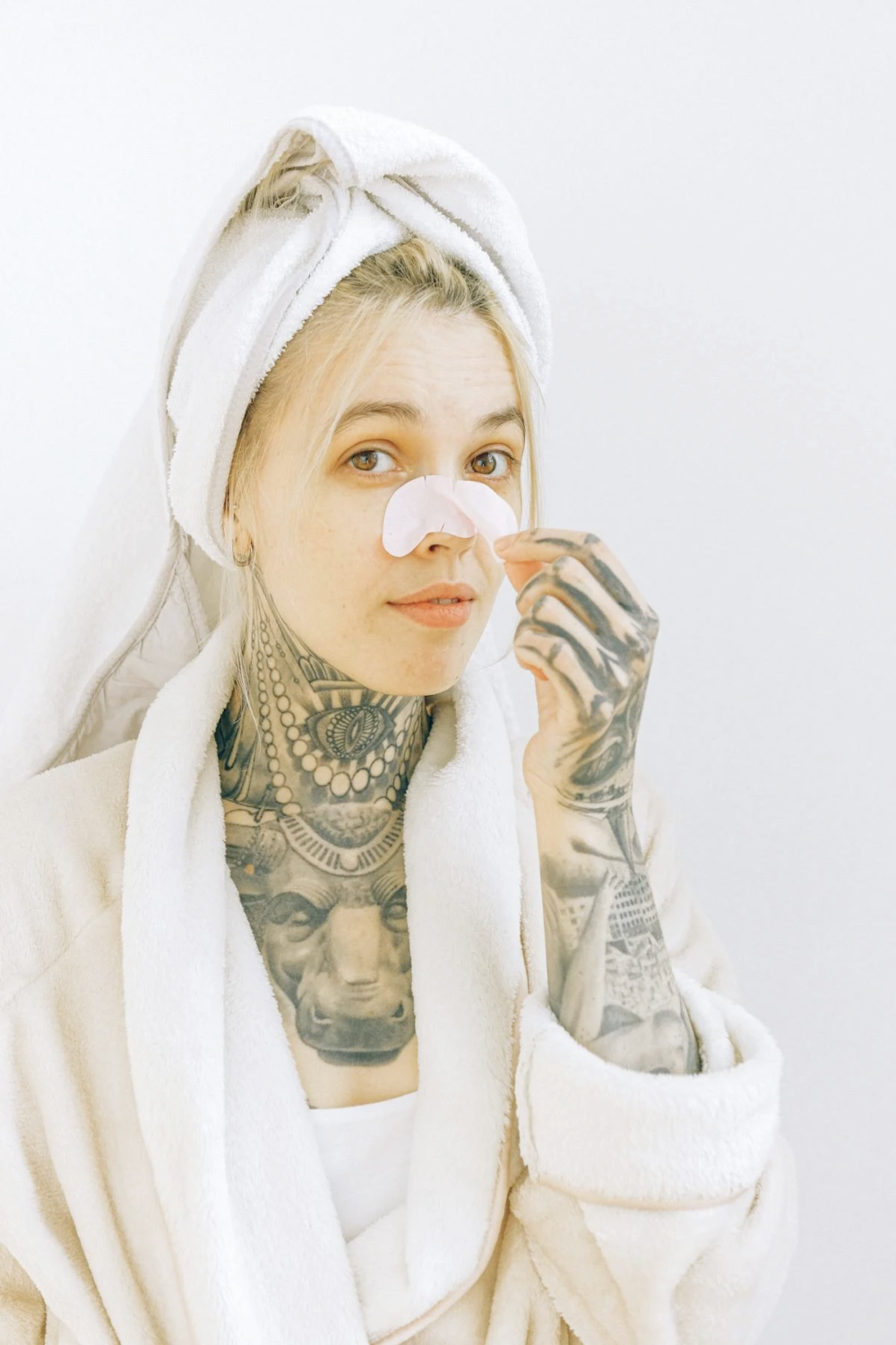 a woman with tattoos applying removing a blackhead nose mask