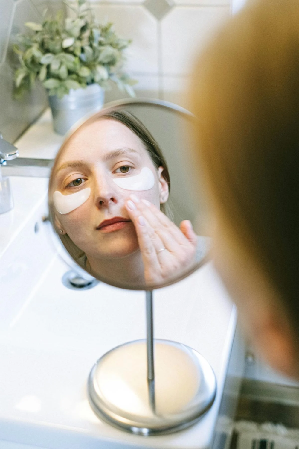a woman with under eye patches looking at a small round mirror