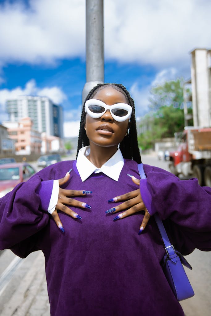 Photo of a Girl Wearing White Sunglasses and a Purple Blouse in a City