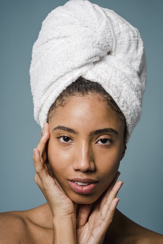 Young African American female with perfect skin and towel on head touching face and looking at camera after shower